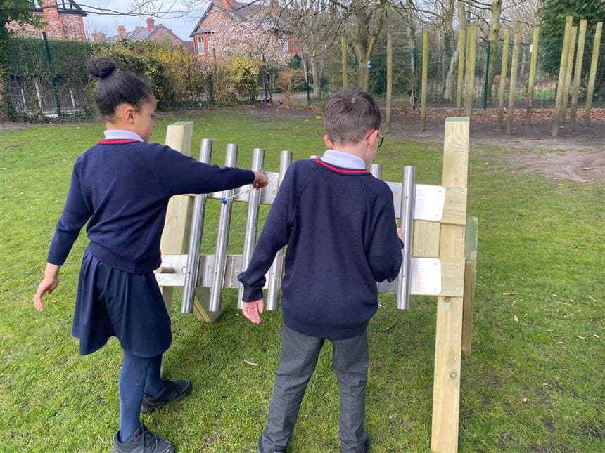 two young children playing on the freestanding chimes in their playground