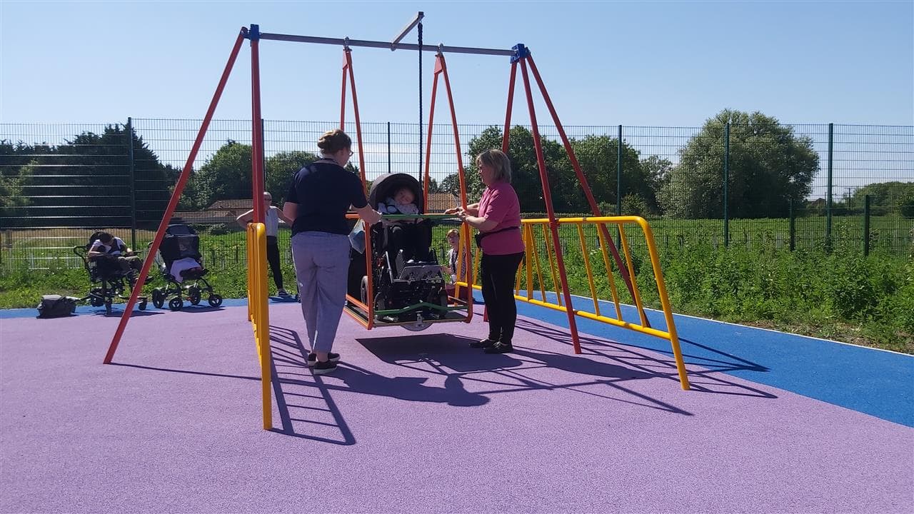 a child playing on our wheel chair swing, adults pushing them