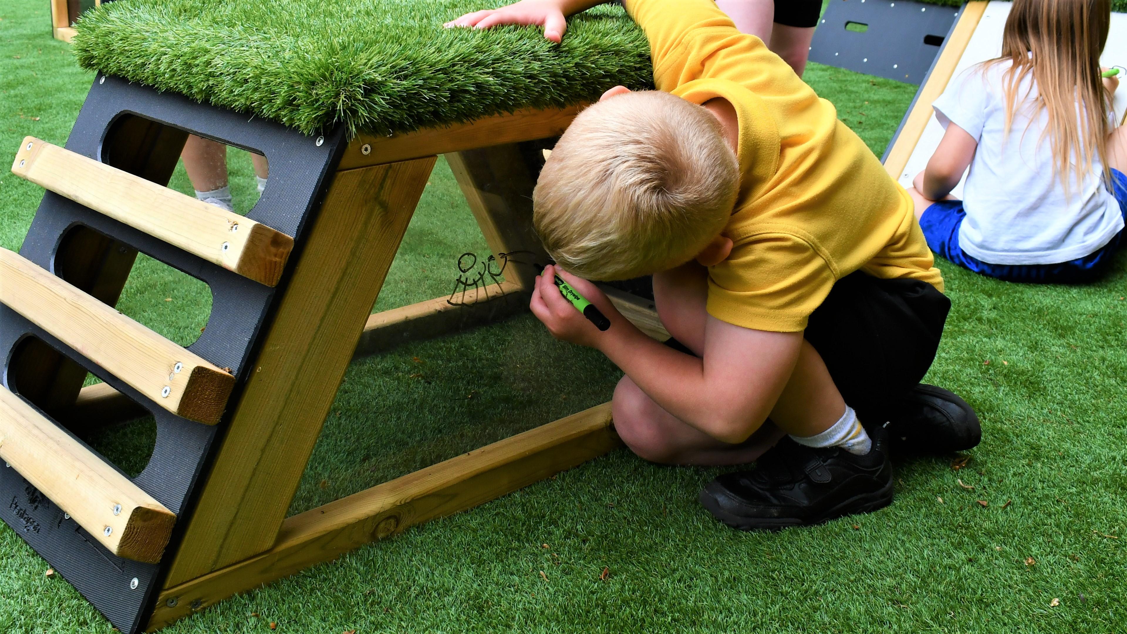 A young boy drawing on the side of the artificial grass top block