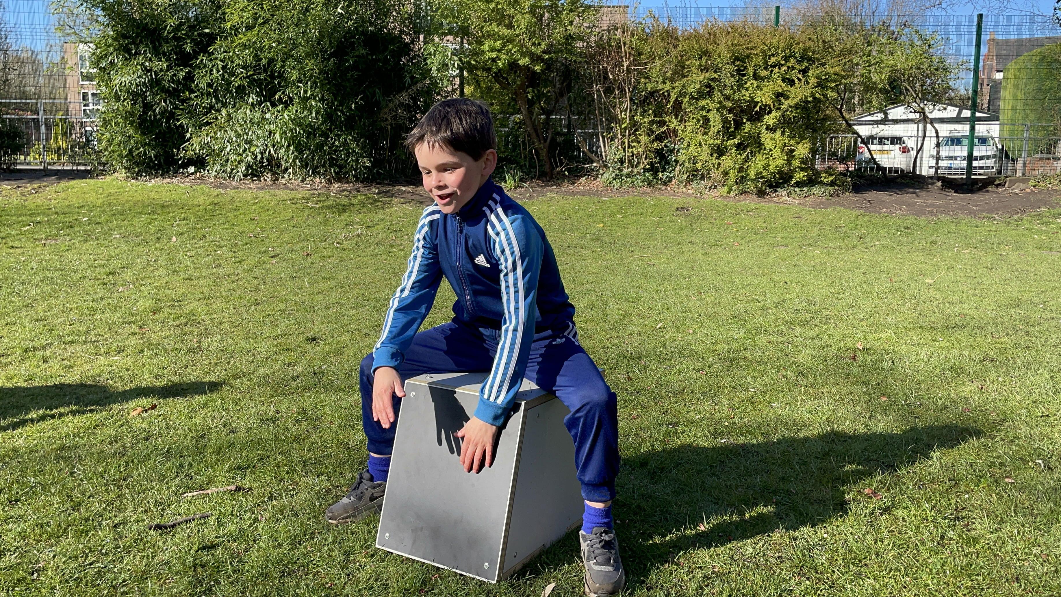 Boy in a school playground making musical sounds sat on a Drum Seat 