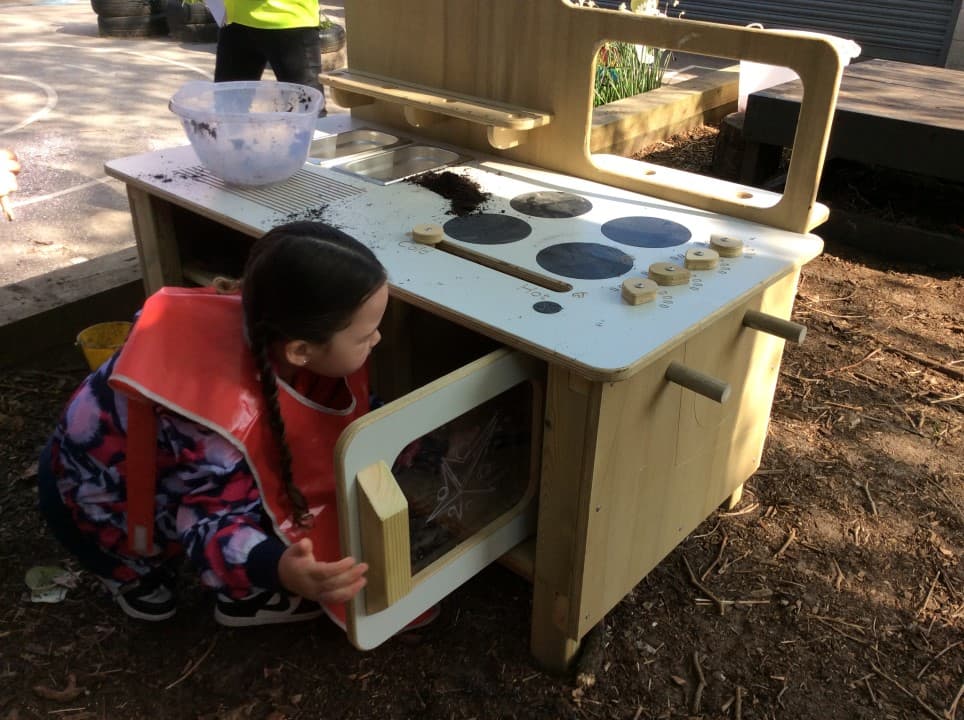 Young girl opening the oven door of the EYFS Mud Kitchen