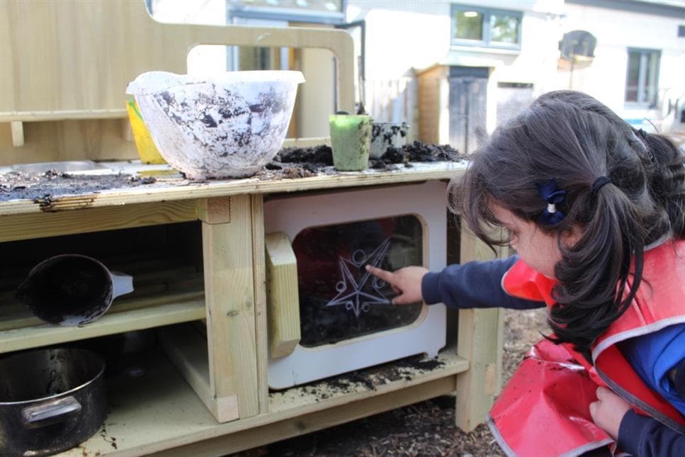 A young girl pointing into the mud kitchen door in her playground