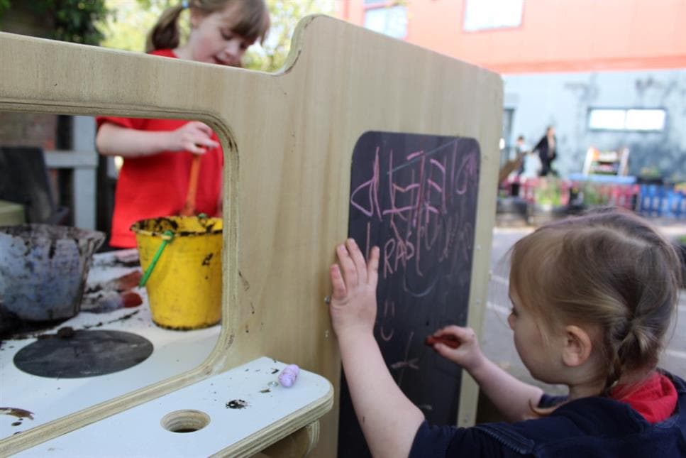 A young girl writing on the chalk board on her mud kitchen in her playground