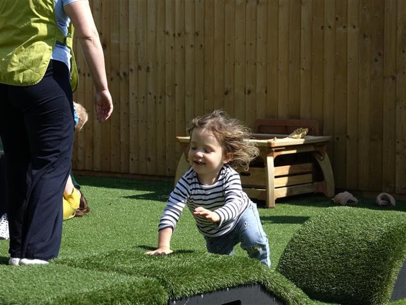 A young girl crawling across the block in their playground
