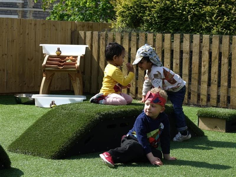 Nursery children playing on grass-topped Get Set, Go! Blocks in the playground.