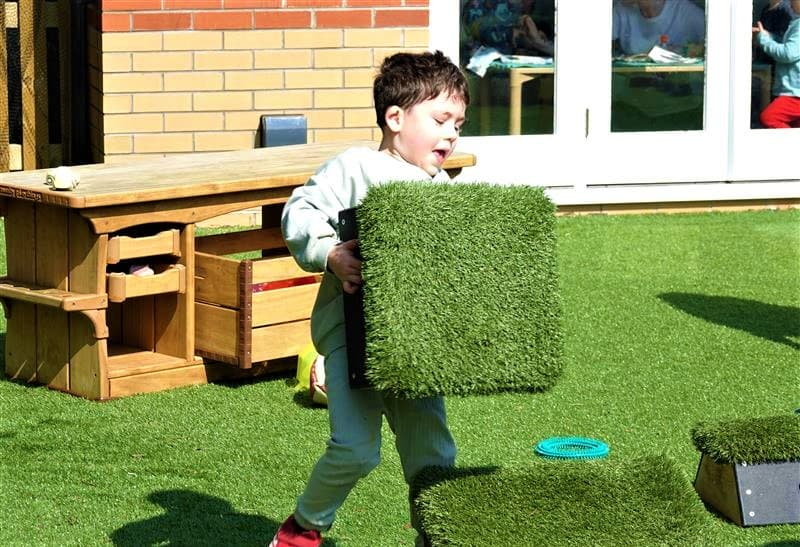 A young boy carrying a movable block in his playground