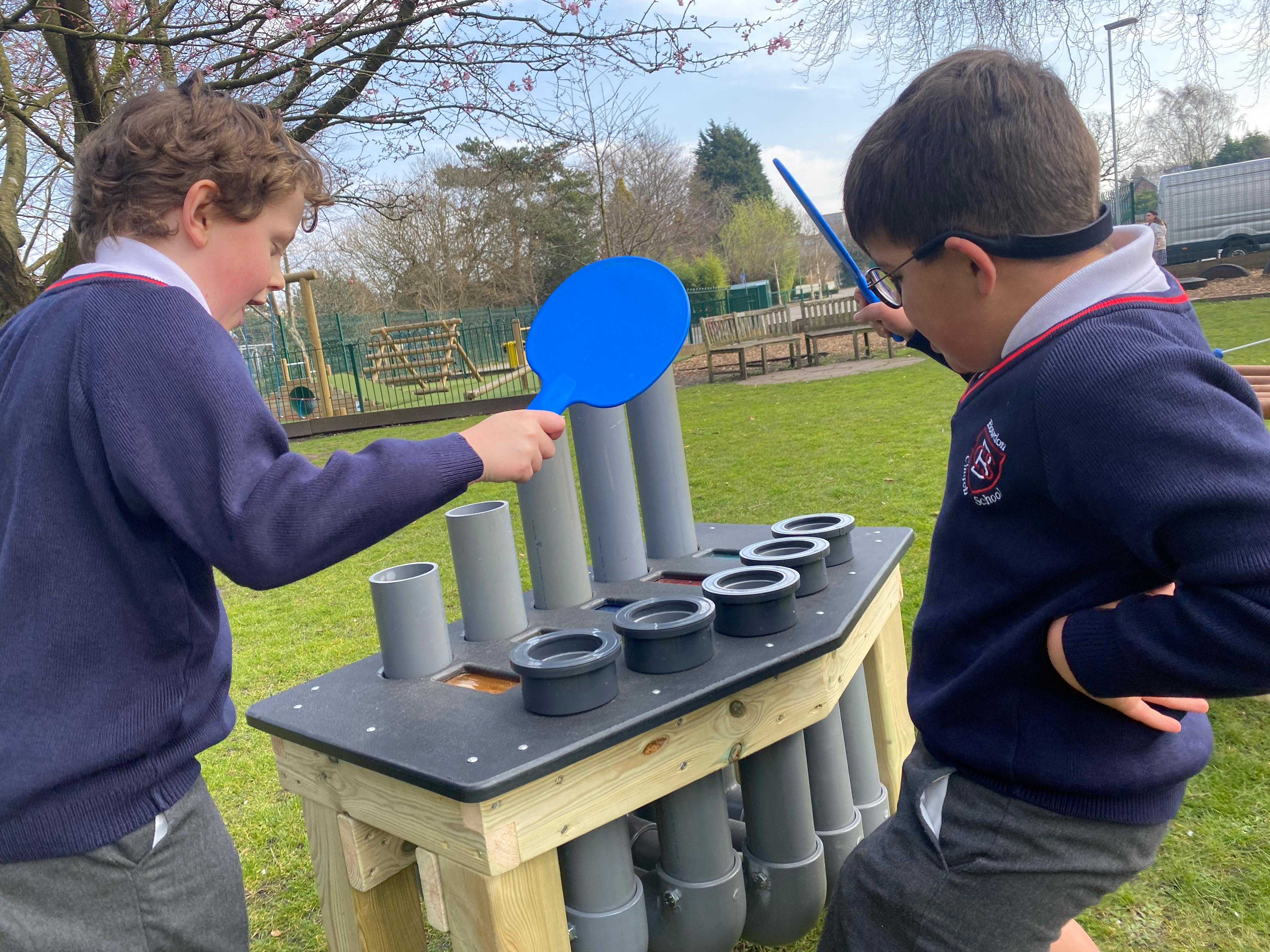 2 children playing on a musical instrument using blue panels to hit the tubes
