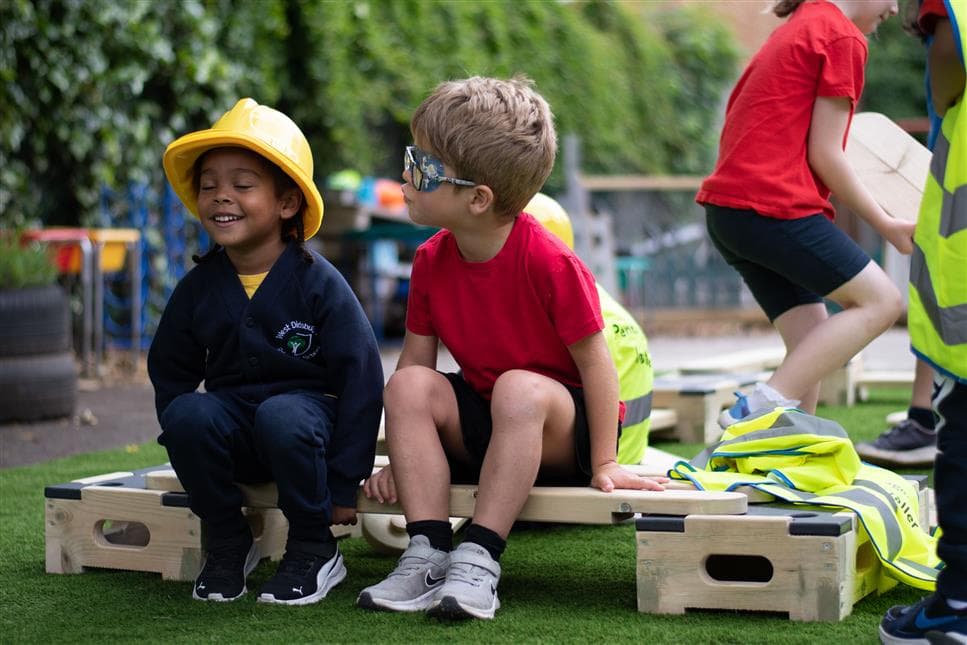 A young boy and girl sitting on one of the planks on the play builder