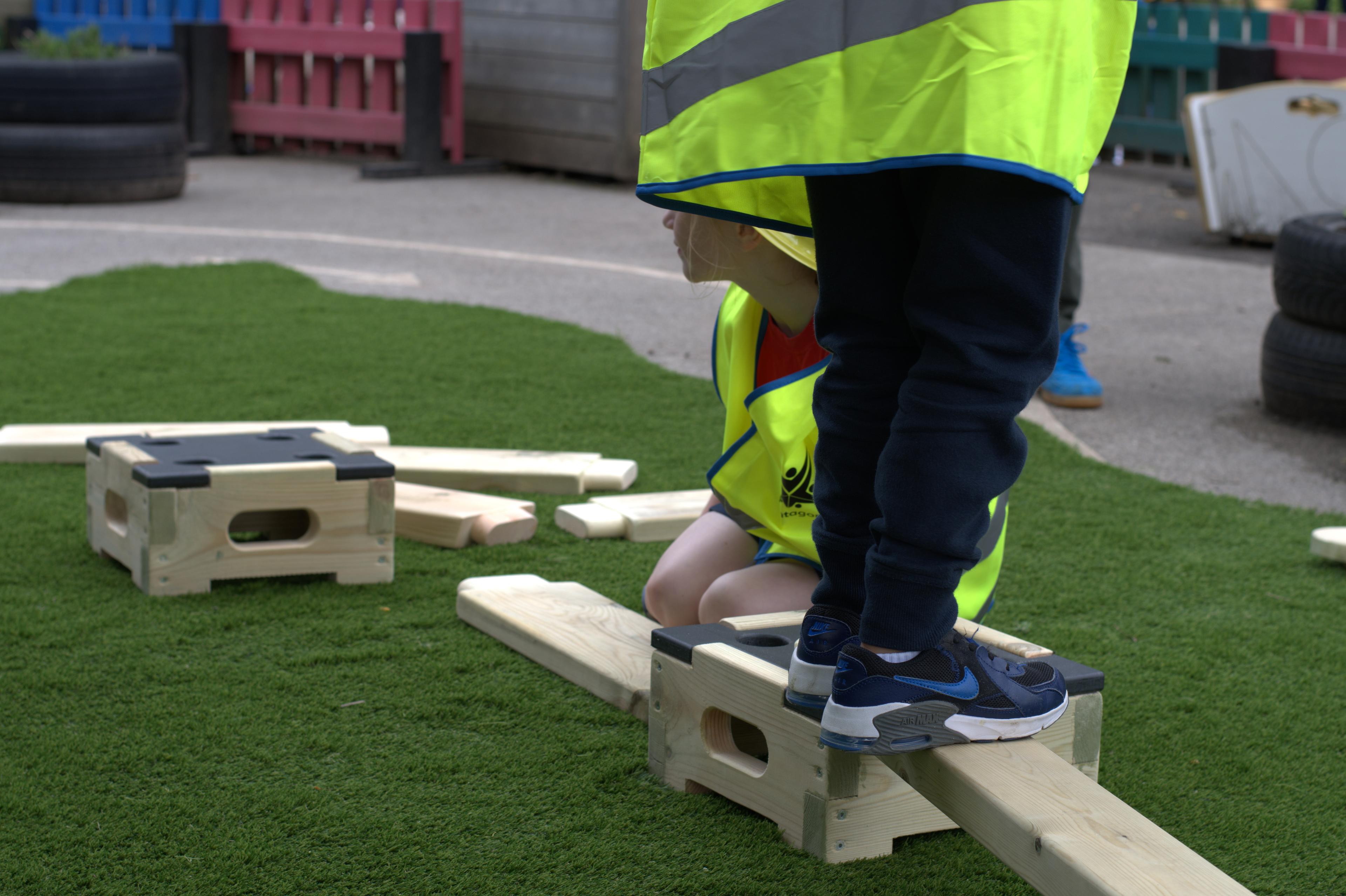 2 children walking across a plank on the play builder