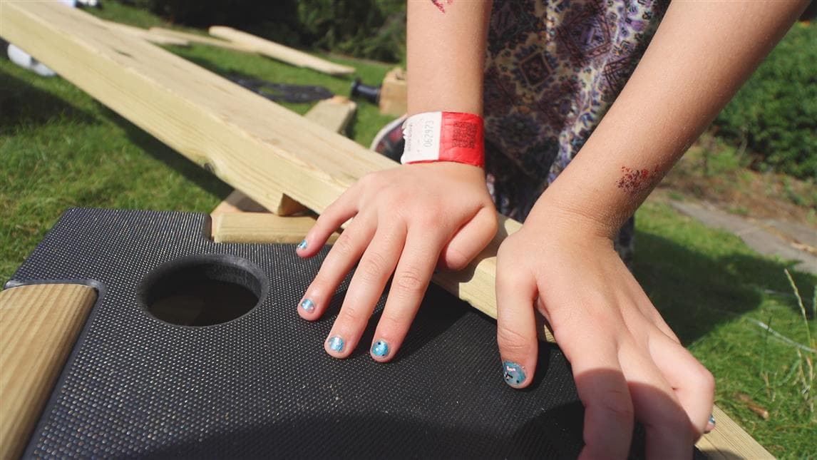 A close up of a girl slotting the plank into the button hole on her construction play equipment