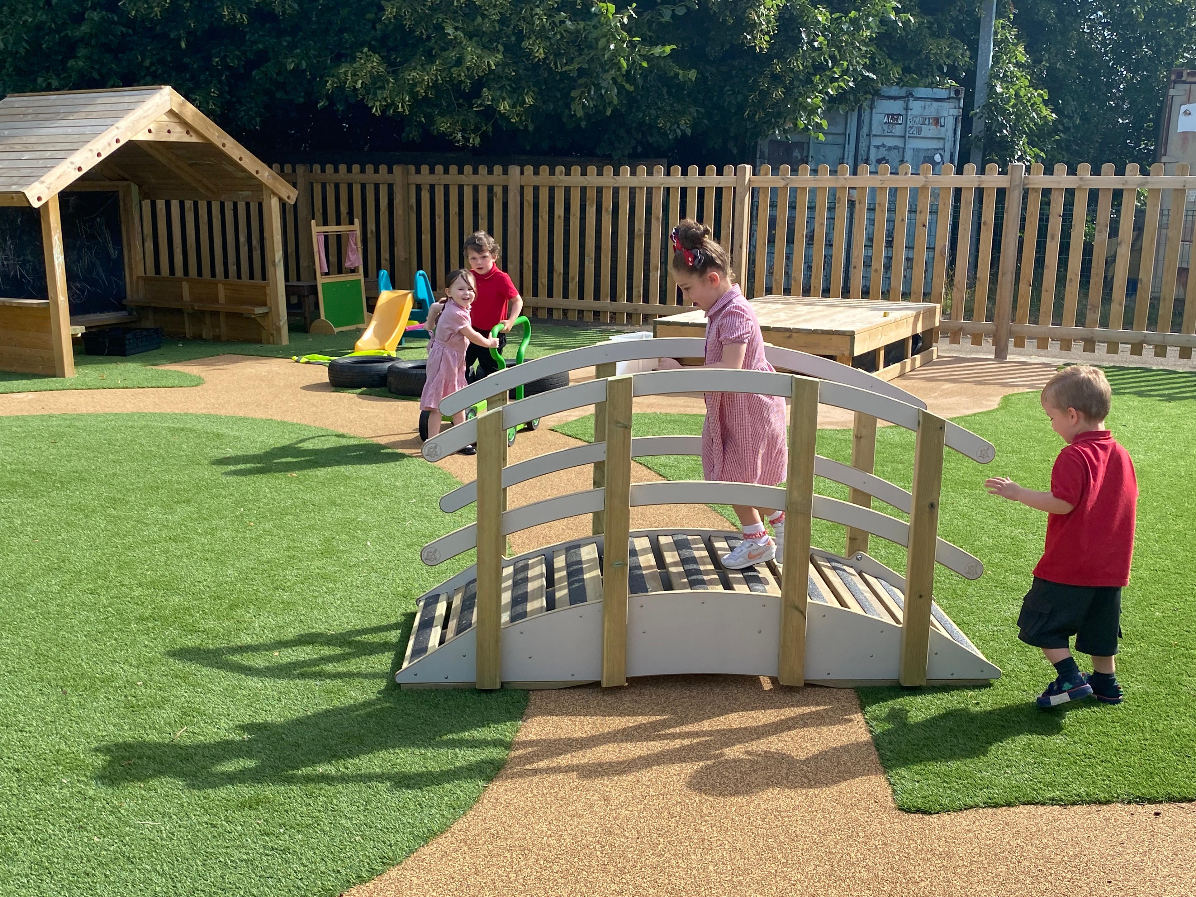 Two children walking across the playridge whilst two children are in the background smiling at them.