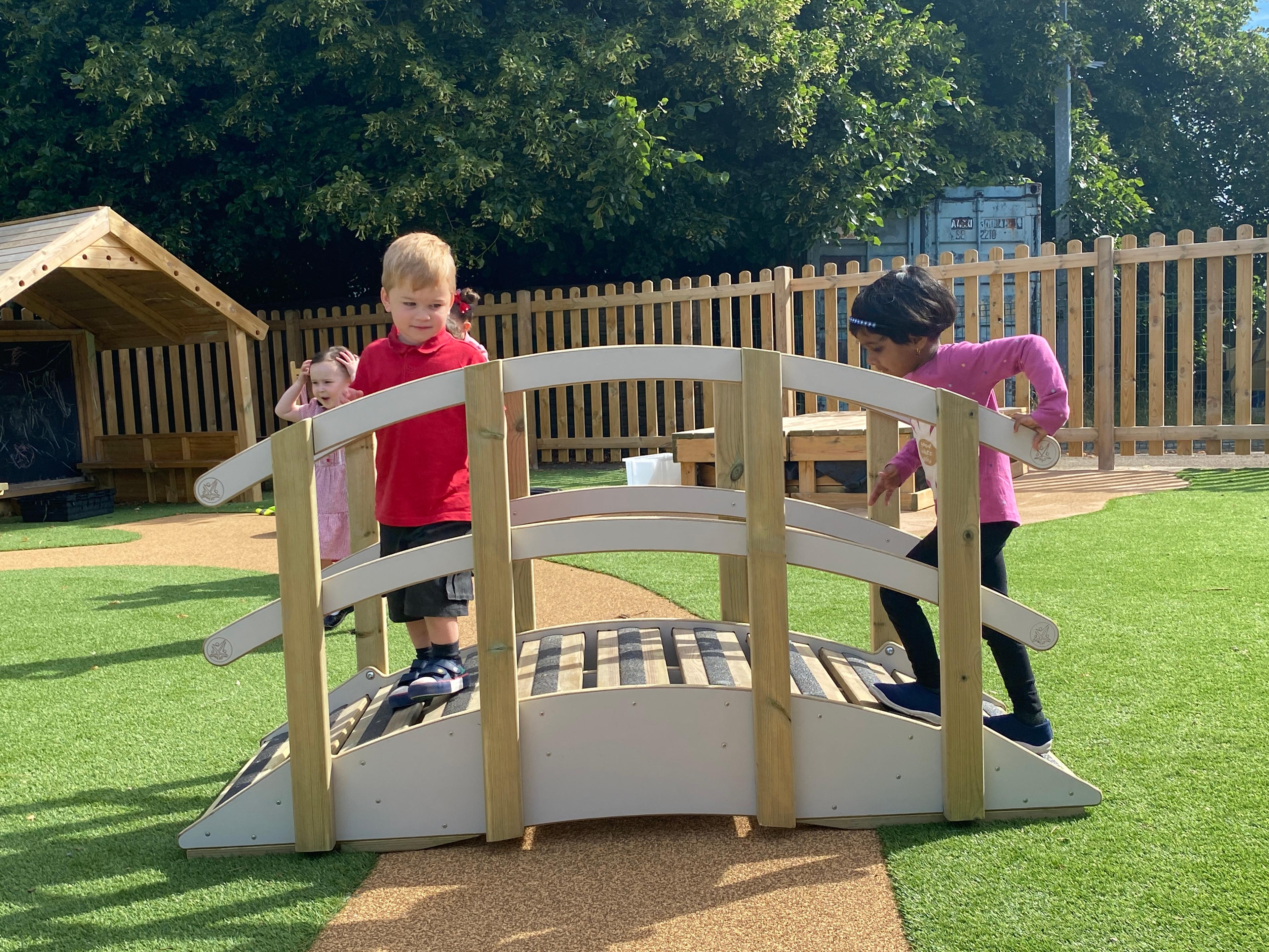 Two eyfs children walking across the play bridge, whilst one child is stood behind