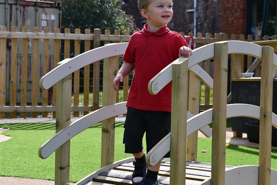 A young boy walking across the play bridge looking to the side, he is wearing his school uniform. 
