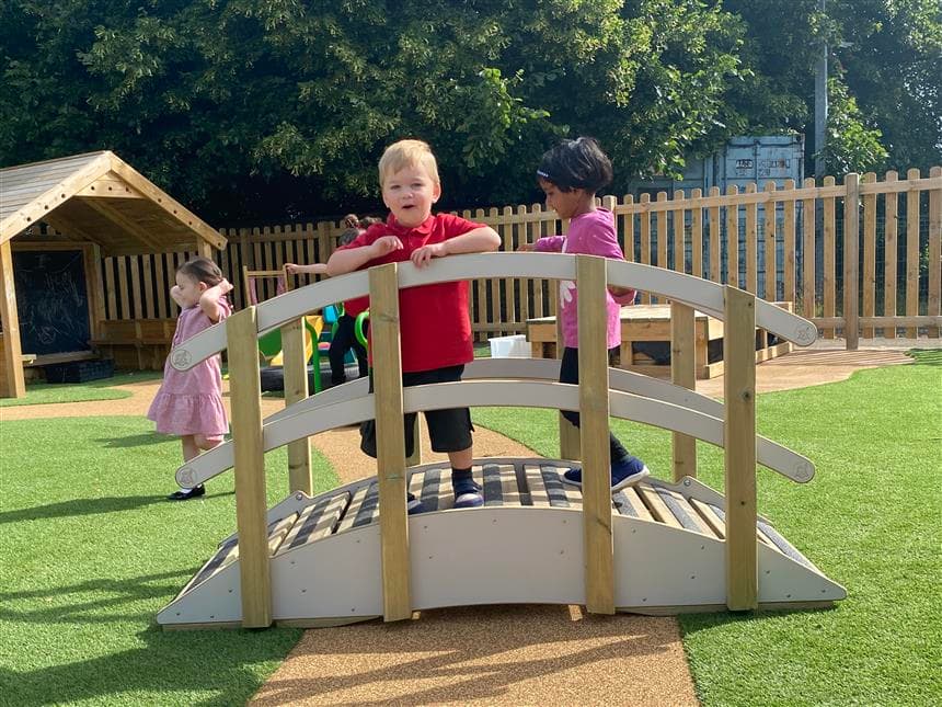 2 young children climbing across the play bridge and one young boy is facing towards the camera who is standing on the bridge 
