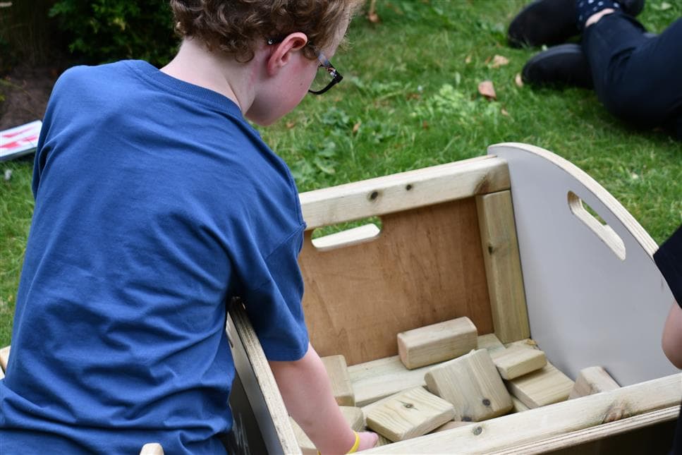 A young boy reaching for the blocks out of the mini skip