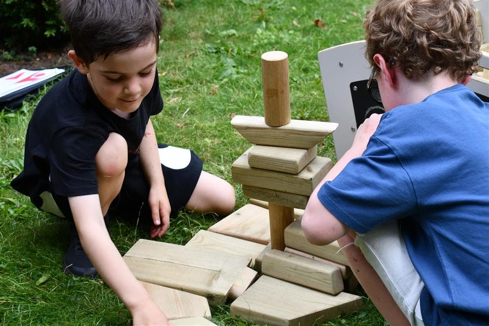 two young boys playing with the blocks from the mini skip they are sat on the grass