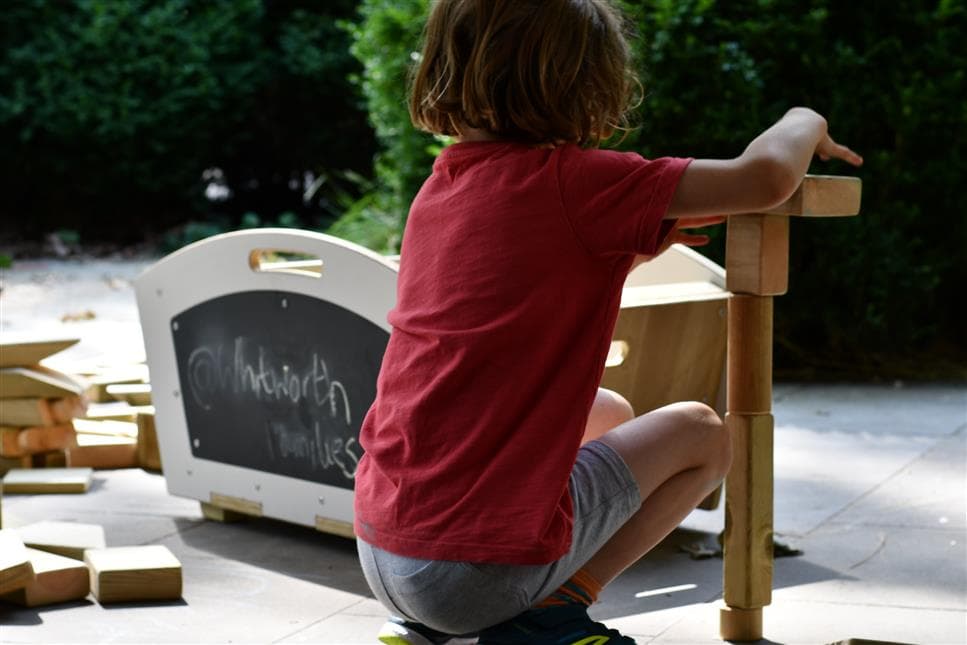 A young boy playing with the blocks from the mini skip he is making a tower in front 