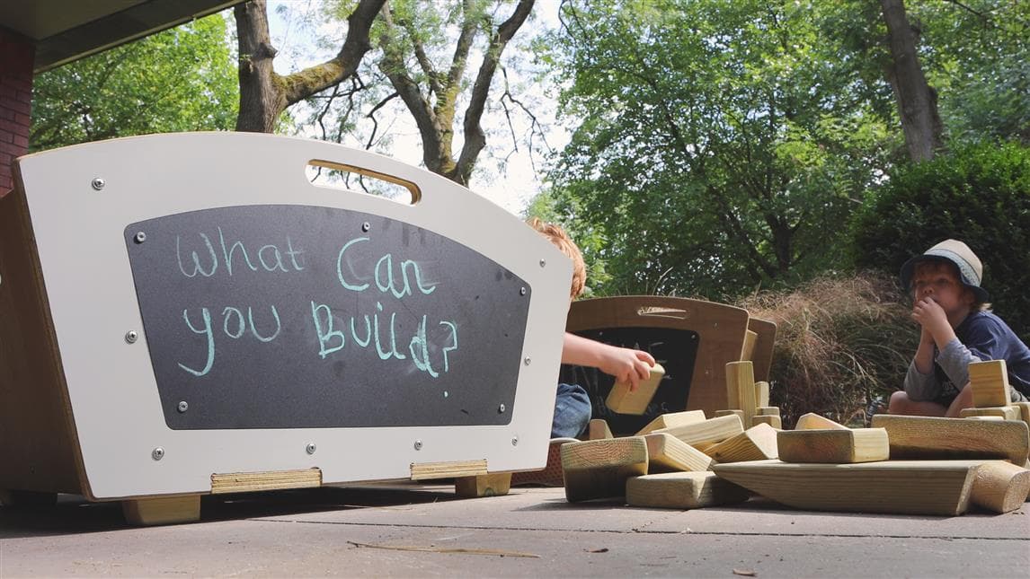 A side view of the mini skip with two young boys playing in the background with the blocks