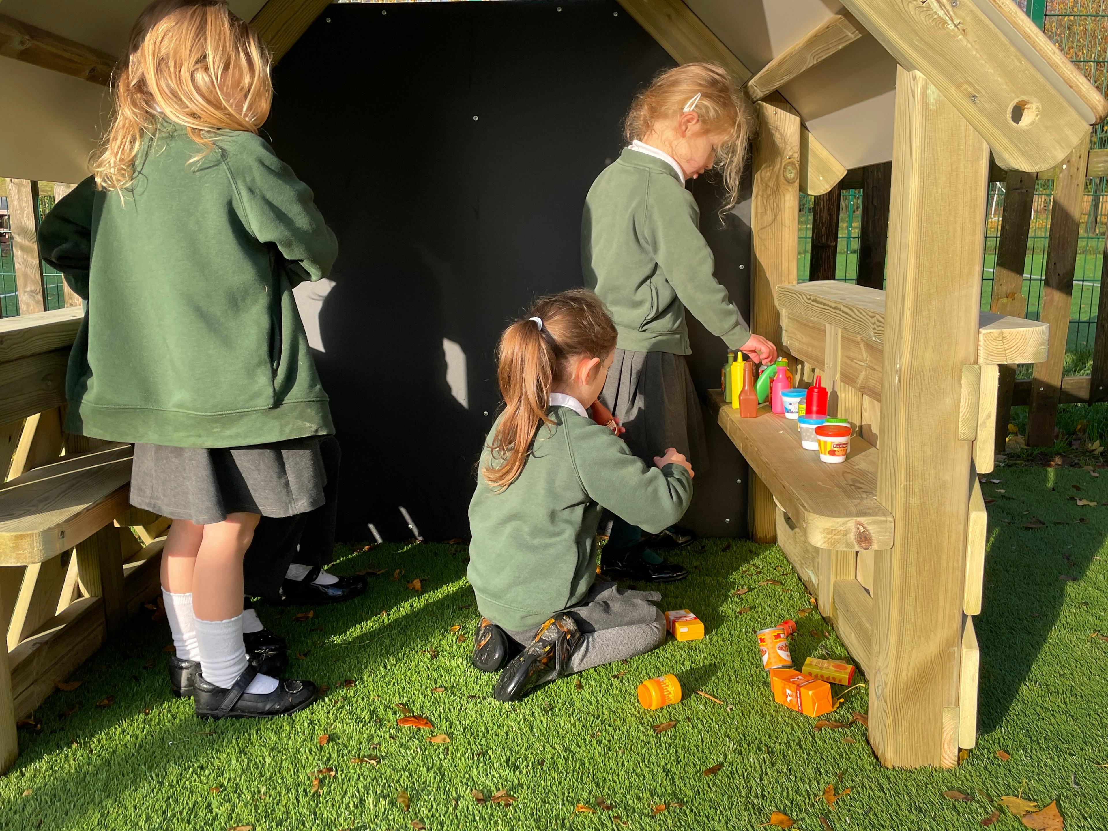children playing in the small playhouse in their playground using role play toys