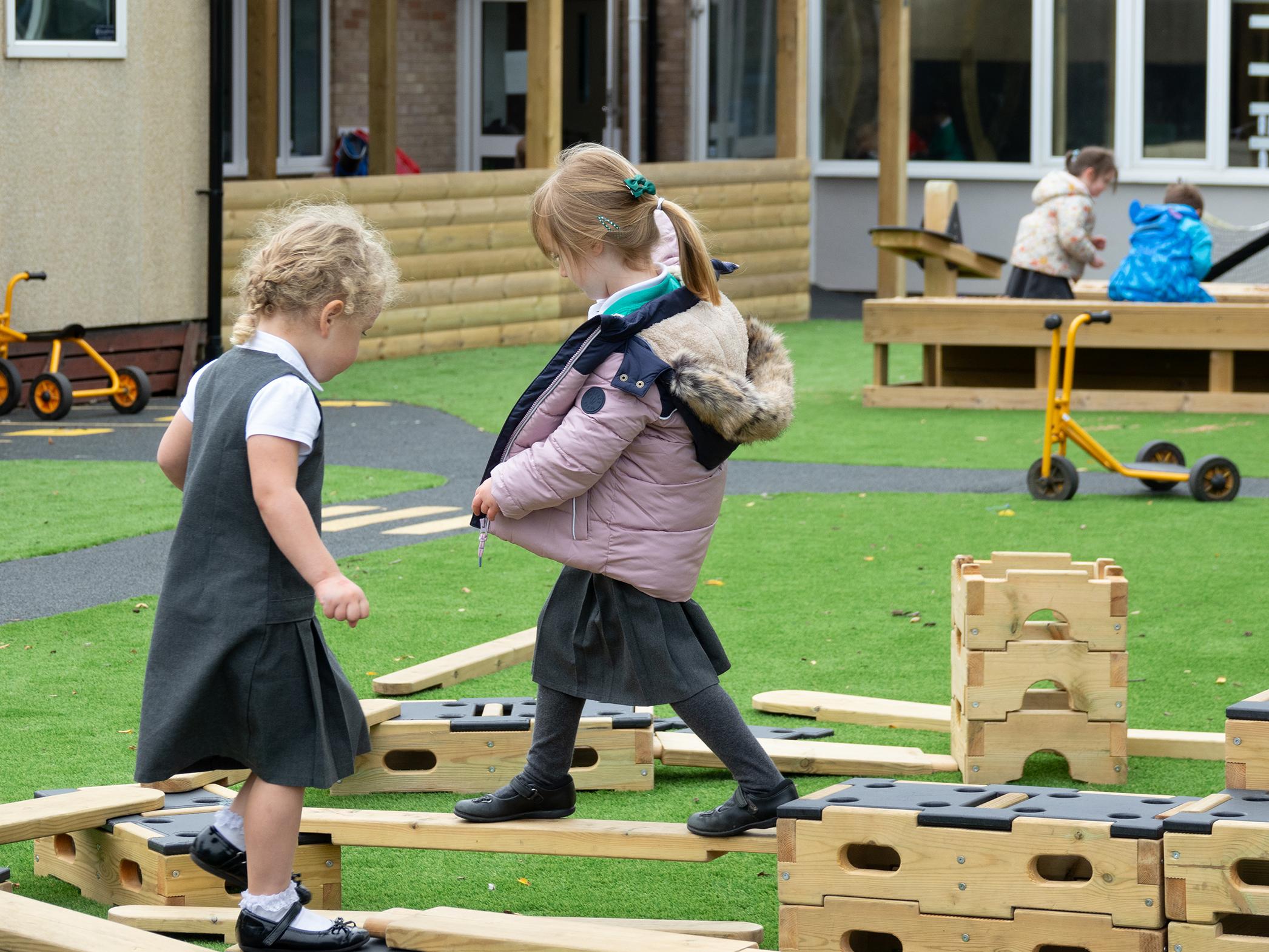 A picture showing 2 children walking on planks which are connected to other parts within the Play Builder Technician Set. Both of the children look engaged and excited to play.