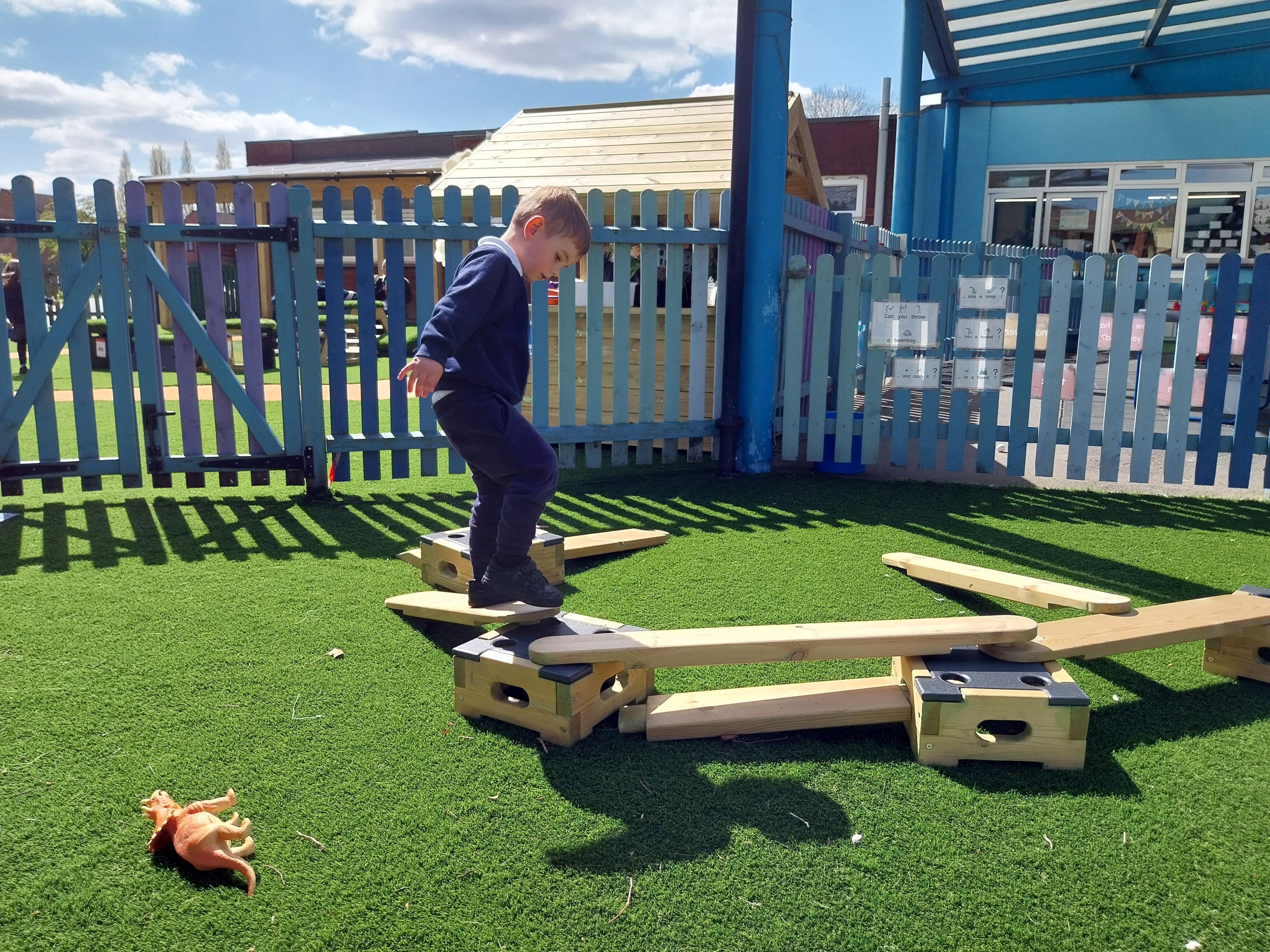A little boy wearing school uniform is trying to complete an obstacle course that has been created from the Play Builder Technician Set. He is currently trying to balance across a wooden plank.