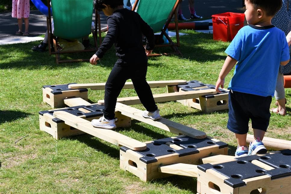 2 young boys playing on the play builder, one young boys is walking across the planks