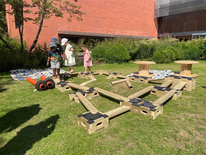 3 children walking over the play builder blocks and planks 