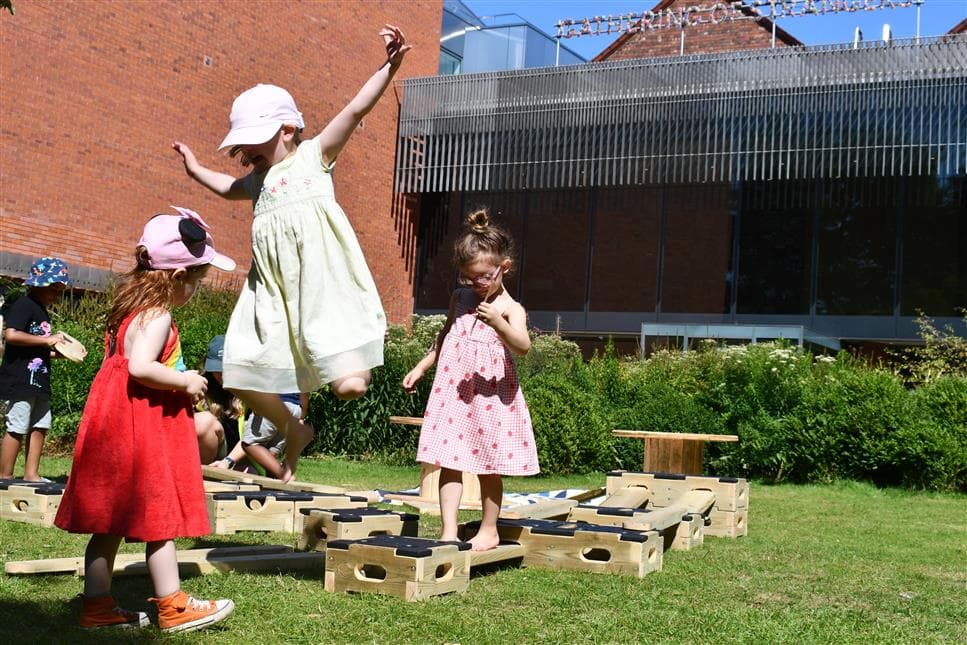 3 young girls playing on the play builder and one young girl is jumping off the end