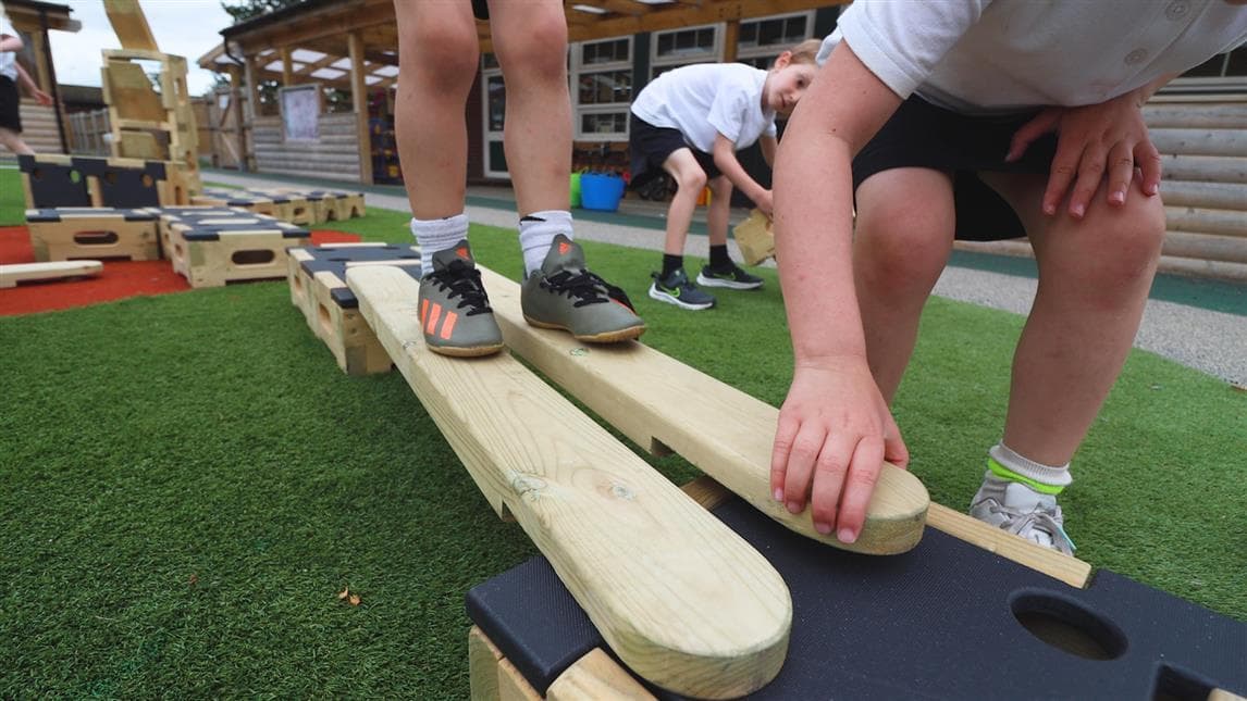 A close up shot of a young boy walking across planks and one young boy is slotting it in