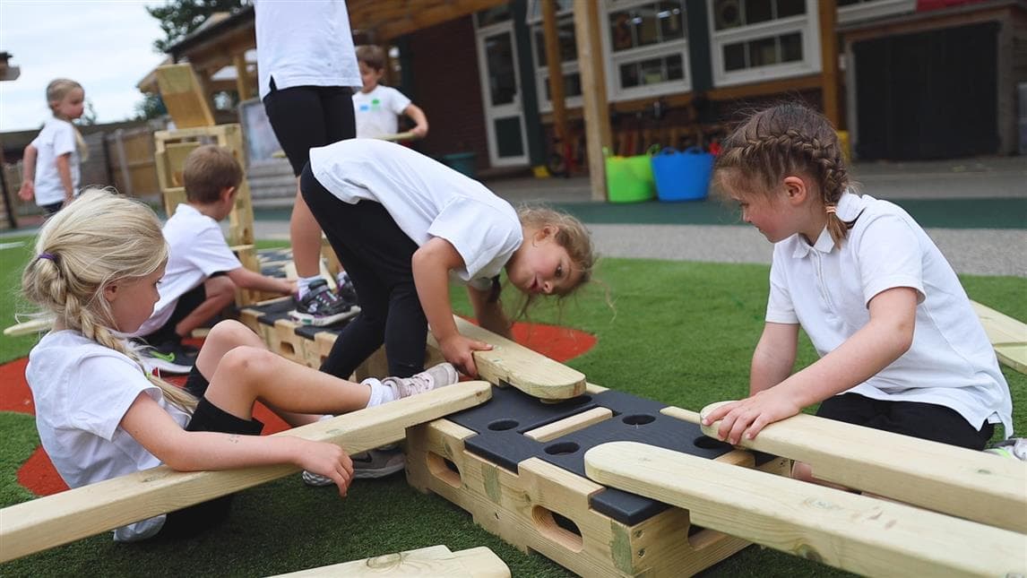3 girls playing with the play builder, one young girl is placing the plank on top of the block