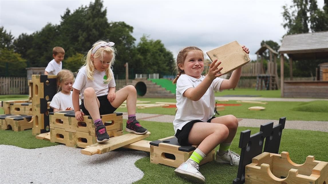 A young girl pretending the play uilder is a car and her friends are riding in the back of the car on the play builder 