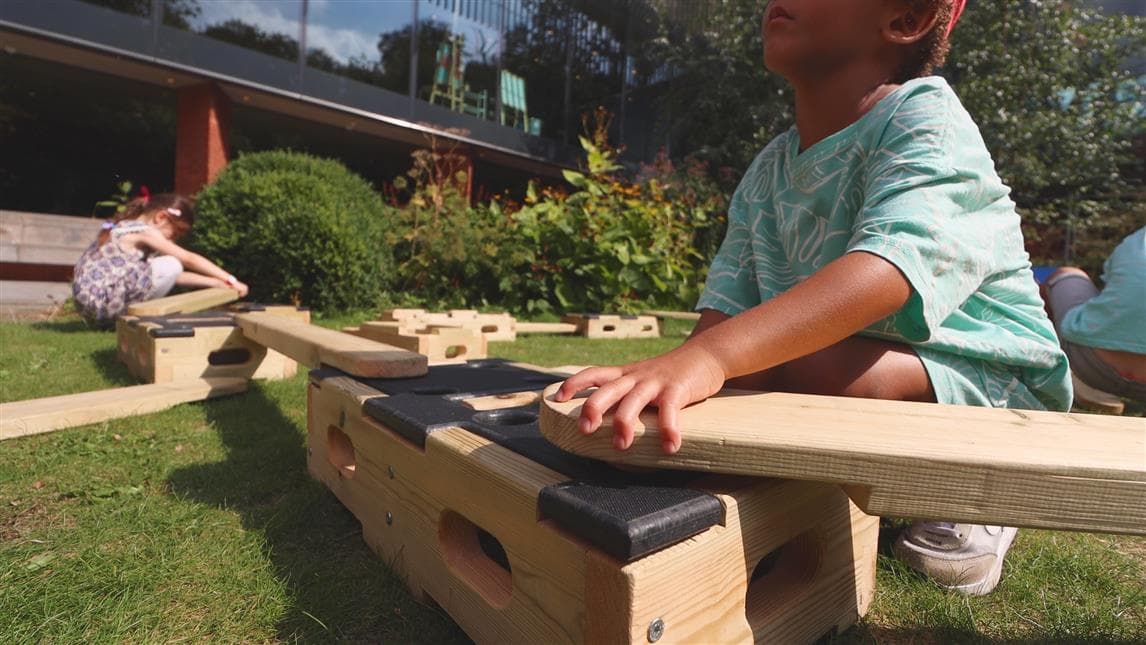 A close up photo of a child slotting the plank onto the play builder