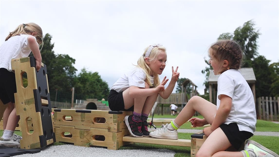 A group of children helping each other to put the planks into the play builder