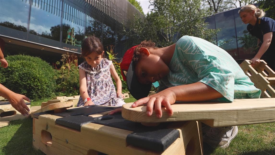 2 children placing the plank on top of the play builder block