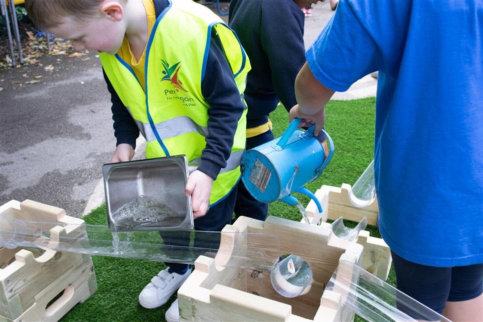 A young boy pouring water water into the channel on the play builder