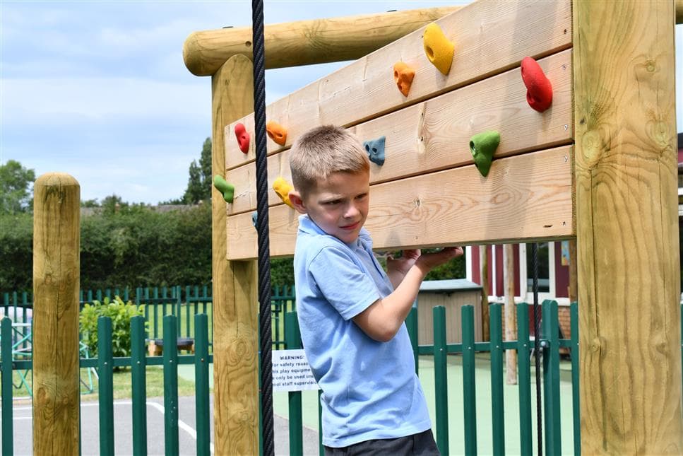 A young boy climbing on the climbing wall on his climbing frame