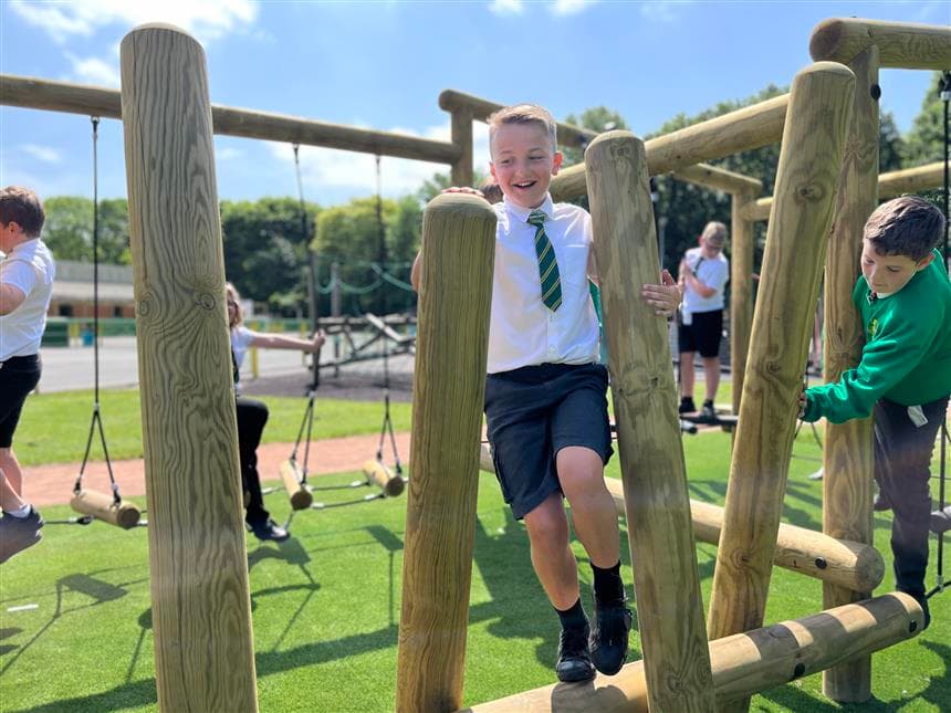 A child walking across wobbly logs on the climbing frame in his playground