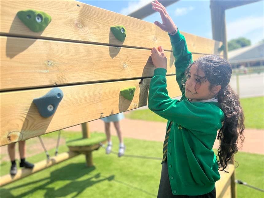 A young girl climbing across the climbing wall in her playground