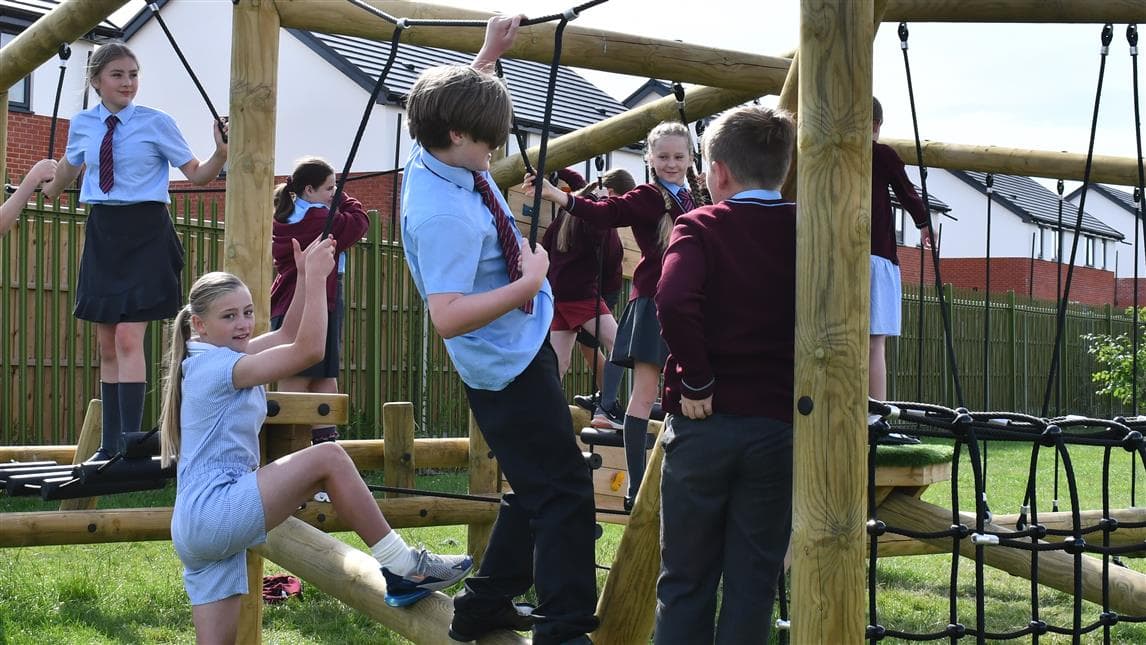 A class of children climbing on the climbing frame in their all tarmac playground