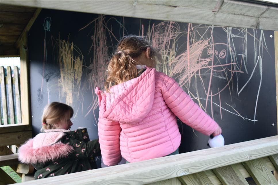 2 young girls drawing on the chalkboard in their playhouse