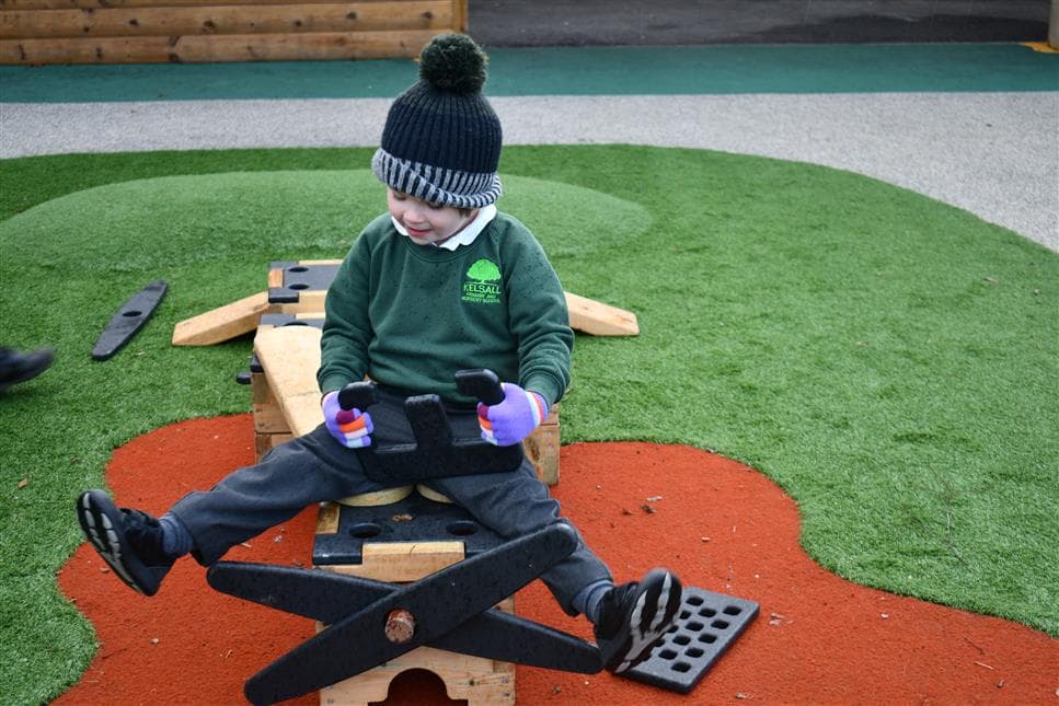 A young boy playing on the blocks pretending to fly a plane in his school playground