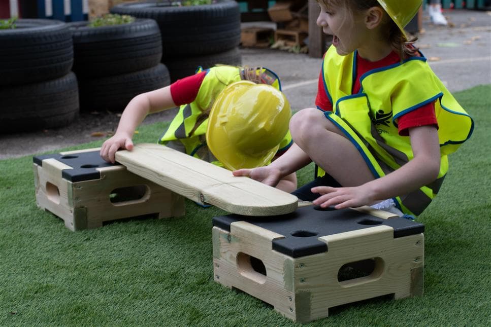twp children placing the plank on the blocks in their playground
