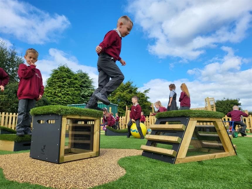 A young boy leaping across the blocks in his playground at school