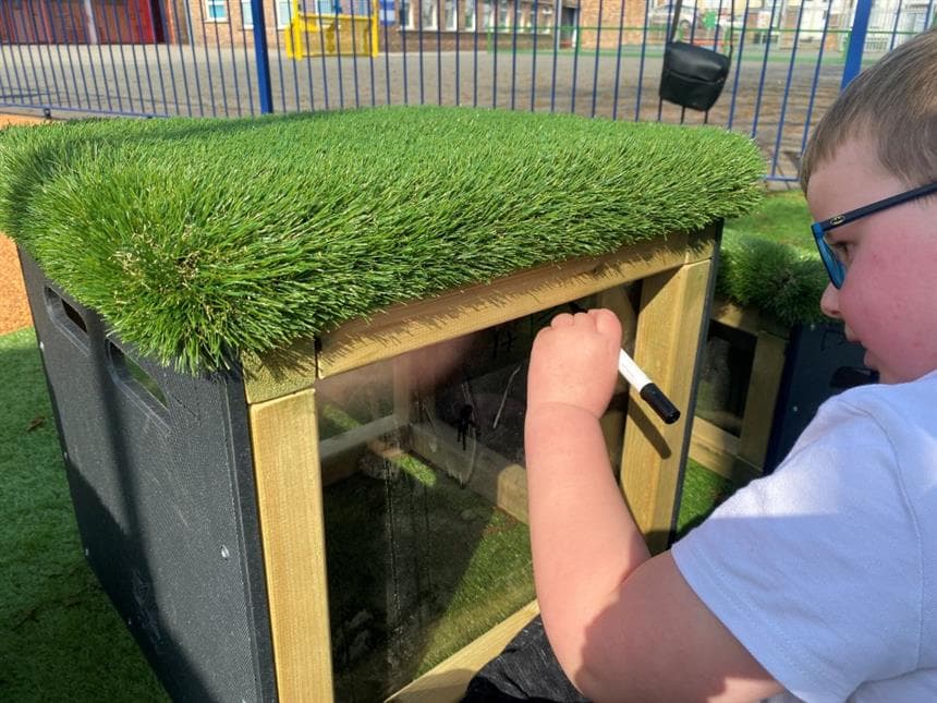 A young boy drawing on the plastic side of the block in his playground at school