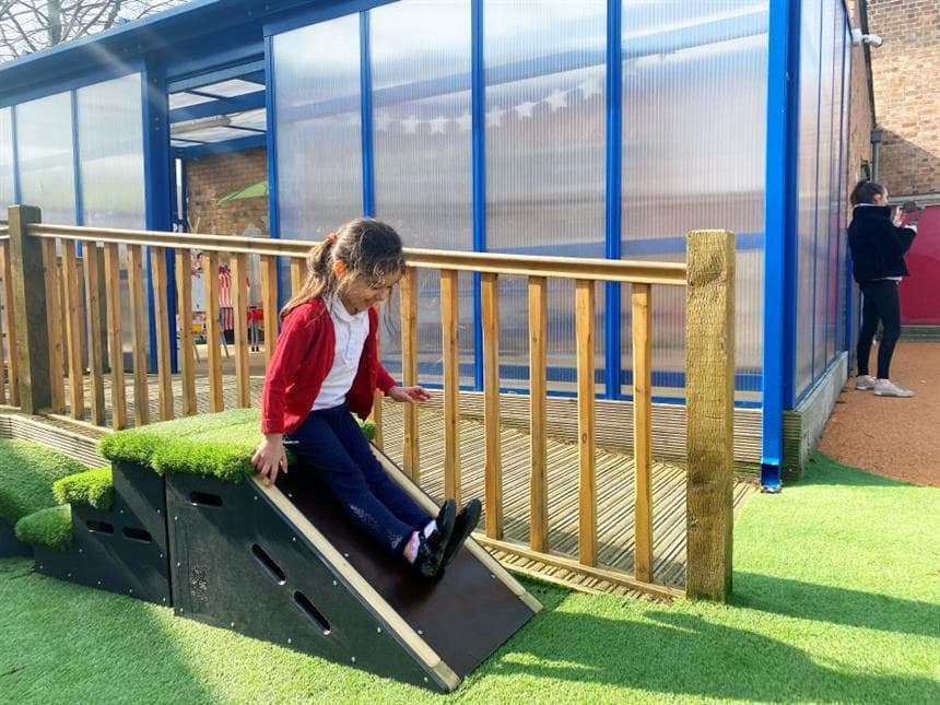 A young girl sliding down the slide on the side of the block in her playground at school