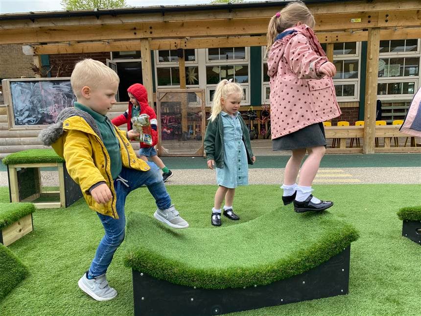 two young children leaping across the blocks in their playground at school