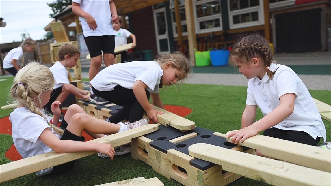 A group of girls placing the planks down on the blocks in their playground