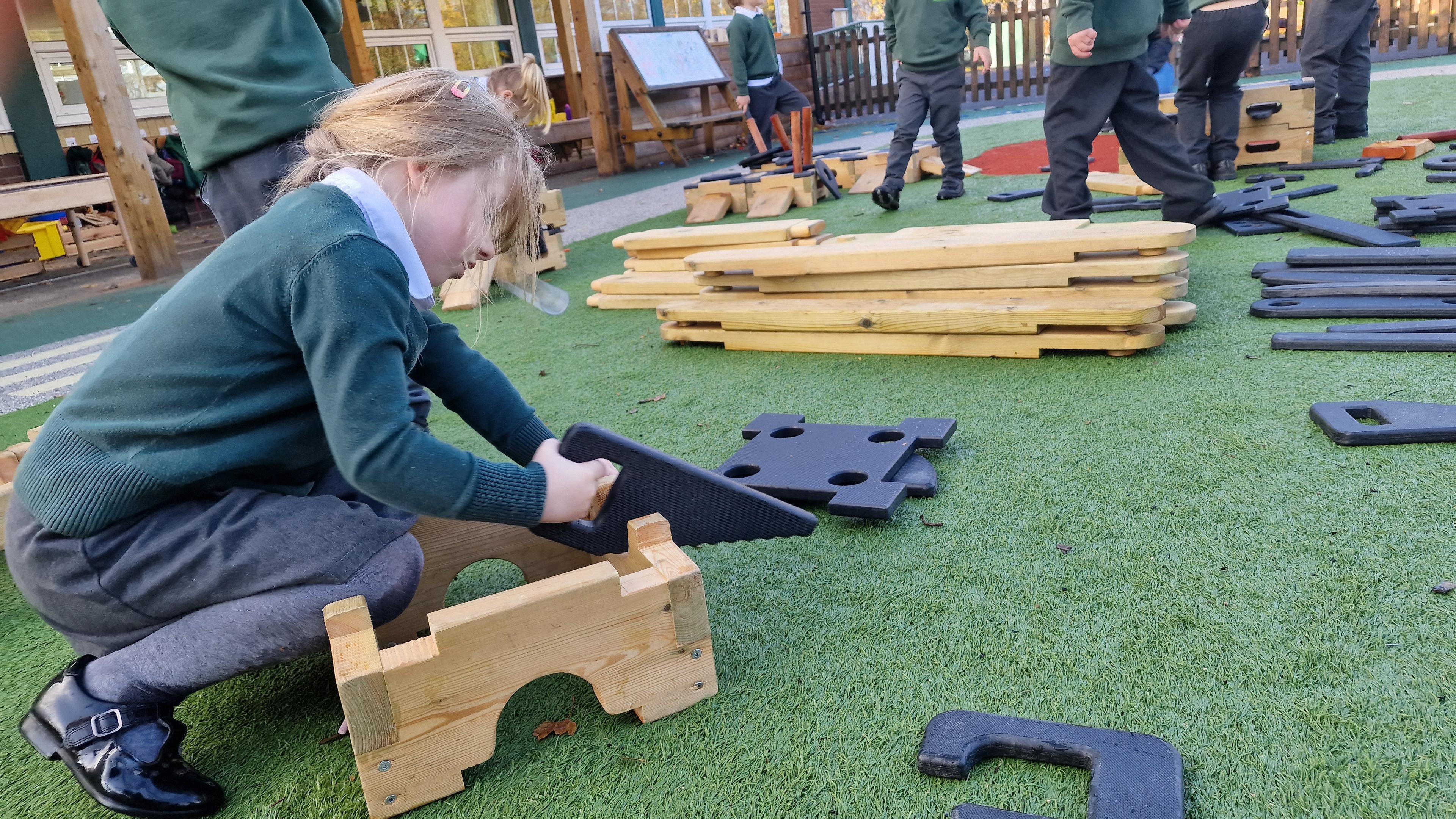 A young girl using the role play saw on the play builder block in the playground