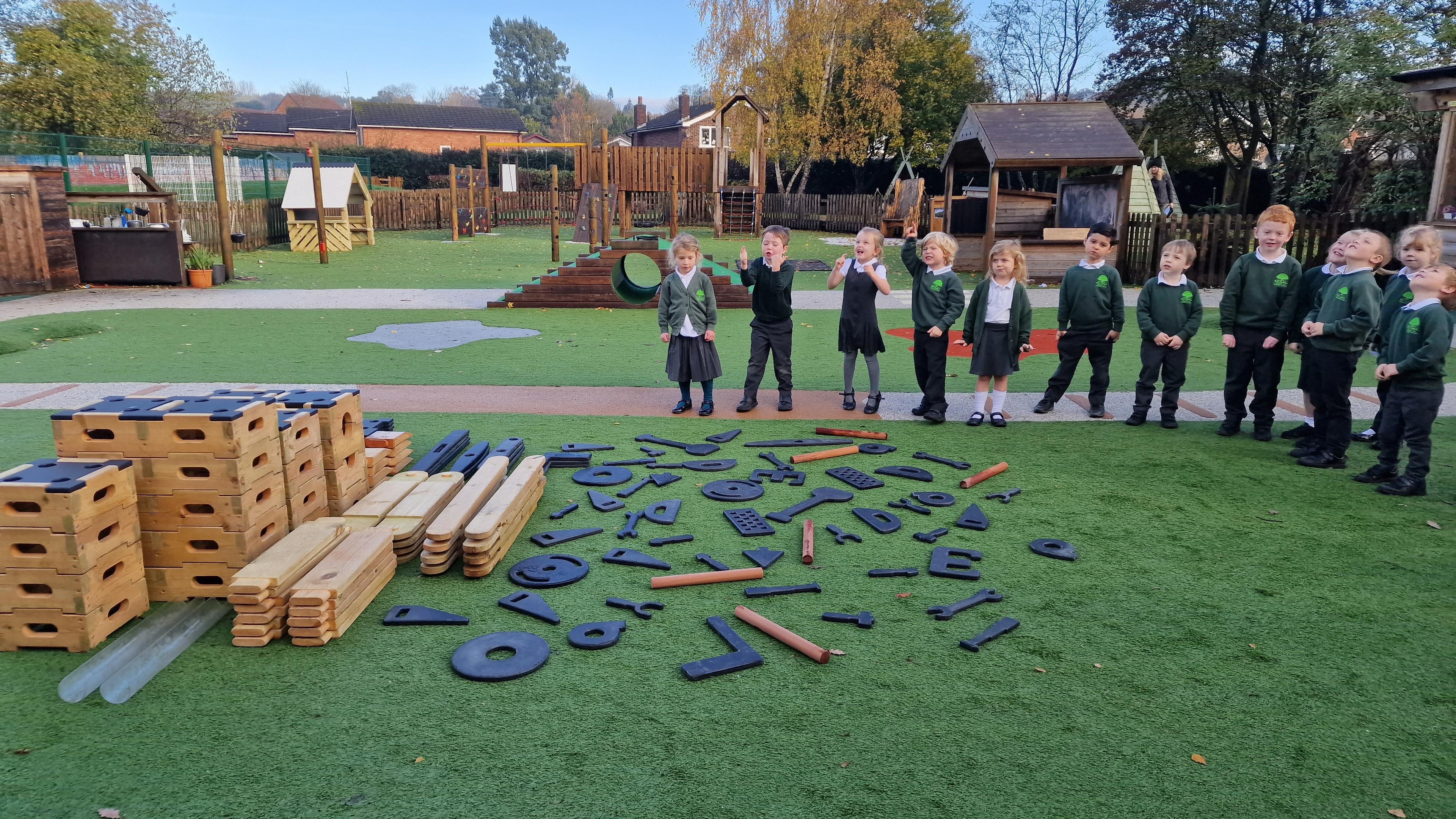 A class of children stood around the play builder set and role play set in their playground