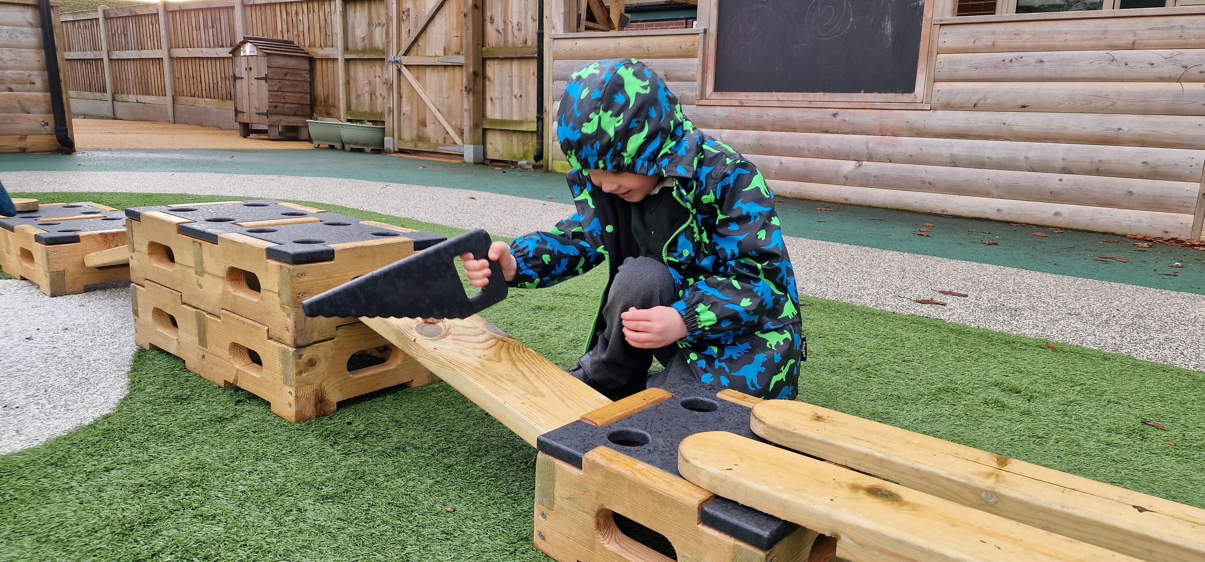 A young boy sawing on a block of wood using the role play addition set